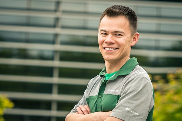 man with short black hair wearing a green and gray polo shirt
