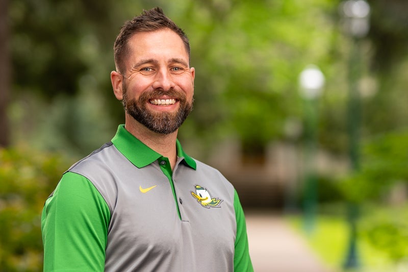 Man with short brown hair and beard wearing a green and gray polo