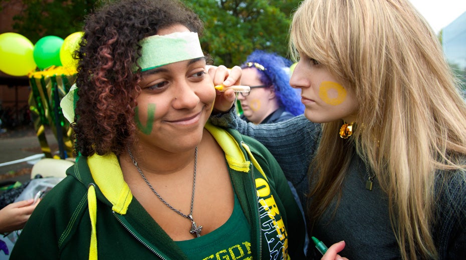 Students using face marker to write UO on face during parade.