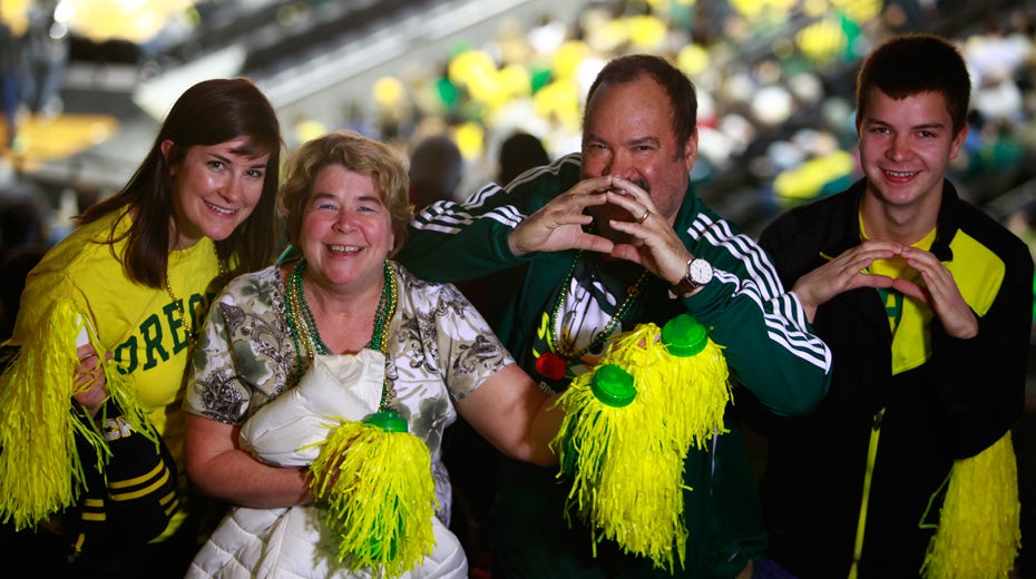 Family wearing Oregon attire at basketball game making "O" with hands.