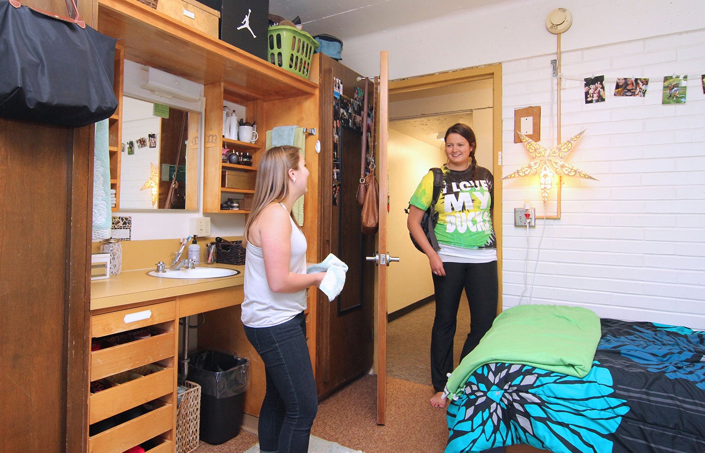 A student stands in the doorway of another students residence hall room and they are happily talking.